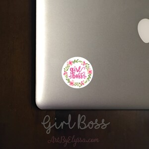 May include: A white circle sticker with a pink floral wreath and the text "girl boss" in pink lettering.
