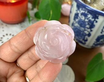 May include: A carved rose made of pink rose quartz. The rose is detailed and has a natural, cloudy appearance.