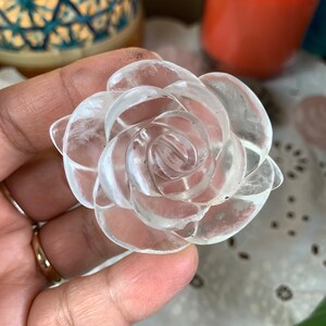 May include: A clear quartz crystal carved into the shape of a rose. The rose is detailed with multiple layers of petals.