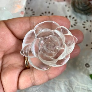 May include: A clear quartz crystal carved into the shape of a rose. The rose is detailed with multiple layers of petals.