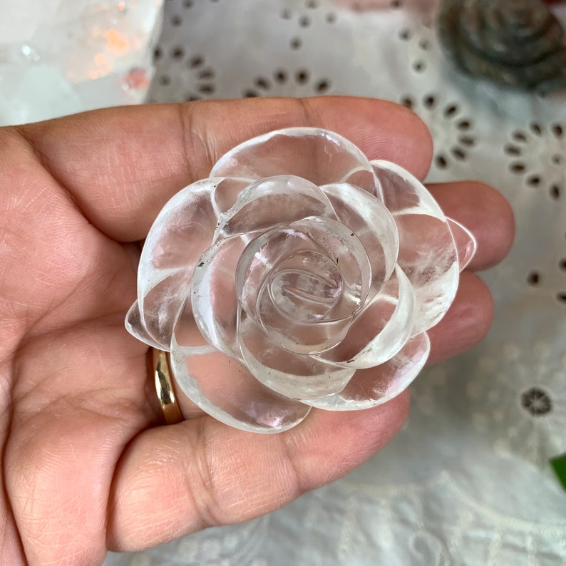 May include: A clear quartz crystal carved into the shape of a rose. The rose is detailed with multiple layers of petals.