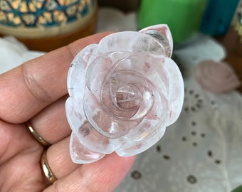 May include: A clear quartz rose carved from a single piece of crystal. The rose is detailed with delicate petals and a center.