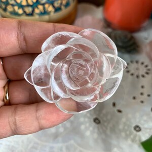 May include: A clear quartz crystal carved into the shape of a rose. The rose is detailed with multiple layers of petals.