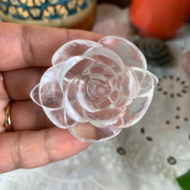 May include: A clear quartz crystal carved into the shape of a rose. The rose is detailed with multiple layers of petals.