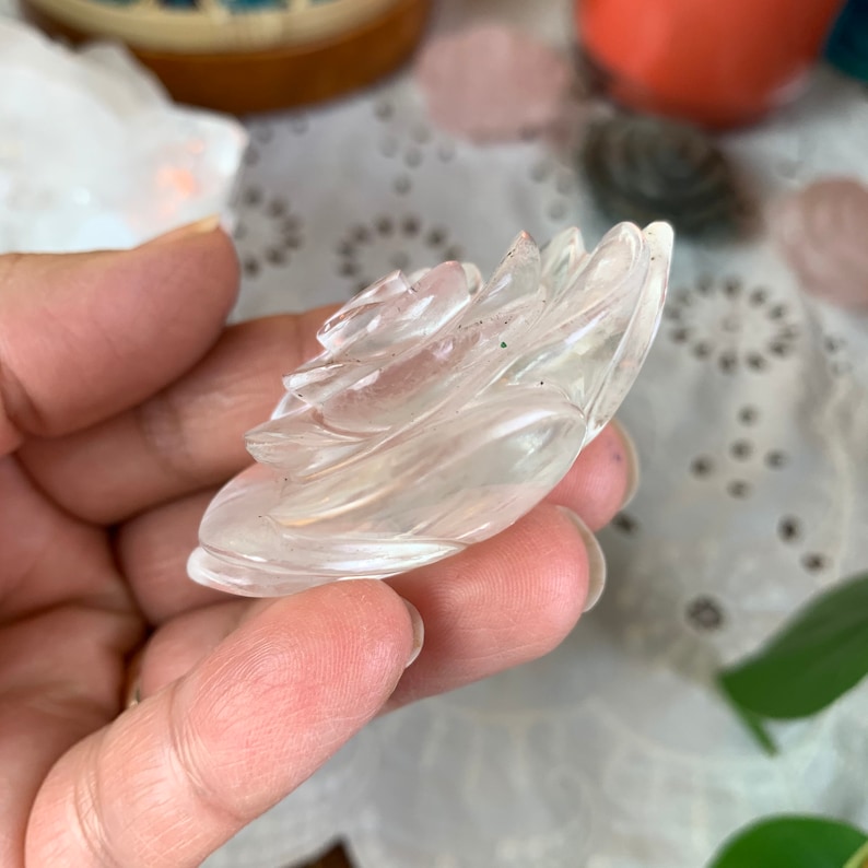 May include: A clear quartz crystal carved into the shape of a rose. The rose is detailed with multiple layers of petals.