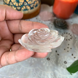 May include: A clear quartz crystal carved into the shape of a rose. The rose is detailed with multiple layers of petals.