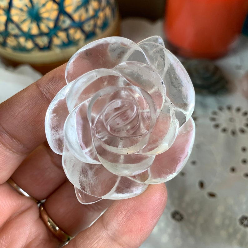 May include: A clear quartz crystal carved into the shape of a rose. The rose is made of multiple layers of petals, creating a delicate and intricate design.