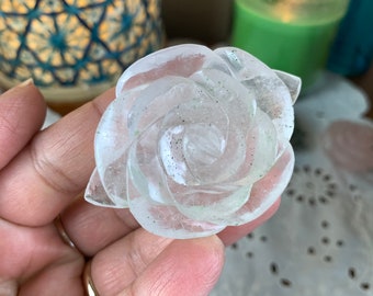 May include: A clear quartz rose carved from a single piece of crystal. The rose is a delicate and intricate design with a natural, cloudy appearance.