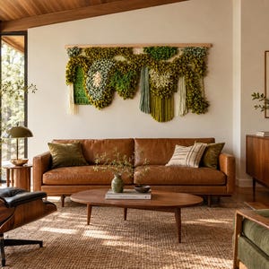 May include: A large, rectangular fiber wall hanging featuring a textured, multi-layered design in shades of olive, sage, and forest green, suspended from a light wood rod. The piece incorporates various yarn loops, knots, and fringe.