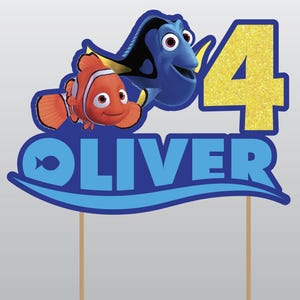 May include: A blue and black Dory and an orange and white Nemo character from the movie Finding Nemo. The characters are on a blue and white wave with the name Oliver and the number 4.