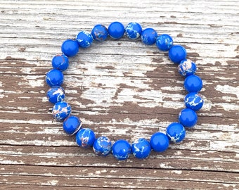 Puede incluir: Un brazalete de jaspe azul y blanco con cuentas redondas. El brazalete está hecho de piedra natural y tiene un patrón moteado.