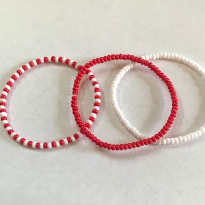 May include: Three beaded bracelets, one red and white, one white and red, and one white. The bracelets are all the same size and are made of small beads.