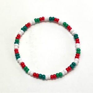 Puede incluir: Un brazalete de cuentas rojas, blancas y verdes. El brazalete está hecho de pequeñas cuentas redondas que están enhebradas juntas en un patrón repetitivo.
