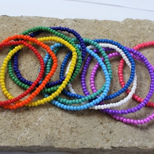 May include: A set of colourful beaded bracelets in a rainbow pattern. The bracelets are made of small, round beads and are arranged in a stack.