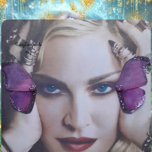 May include: A pair of purple butterfly-shaped earrings with glittered edges and a small central crystal accent. The image features the text FairyLovejewels etsy and Always purchase where you see my name on photo over a portrait of a person.