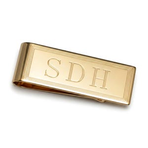 May include: A rectangular gold-toned metal money clip featuring a polished finish and a double-line border engraving. The center of the clip is engraved with the capital letters SDH in a serif font, centered horizontally on the surface.