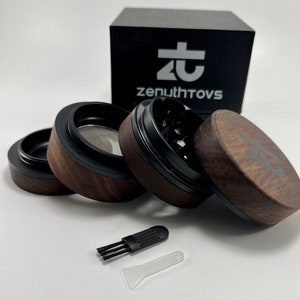May include: A disassembled wooden herb grinder with black accents, a mesh screen, and a cleaning brush. The grinder has a dark wood grain finish and the text "zenuthtovs" is visible on the black box in the background.