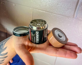 May include: A black and silver battery grinder with the text "DURACELL" printed on the side. The grinder is open, revealing the grinding teeth. A brown and silver battery top is next to the grinder.