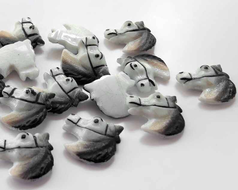 Puede incluir: Una colecci&oacute;n de peque&ntilde;as figuras de cabeza de caballo talladas. Las figuras son principalmente blancas con detalles grises y marrones, y presentan bridas detalladas. Las cabezas de caballo est&aacute;n dispersas sobre una superficie blanca.