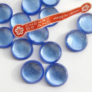 Puede incluir: Una colección de cuentas de vidrio azul iridiscente con una etiqueta que dice "Cherry Brand Made in Japan".
