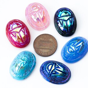 May include: Six iridescent glass scarab beetle charms in various colors, including pink, blue, green, and red. The charms are oval-shaped and feature a detailed scarab beetle design.