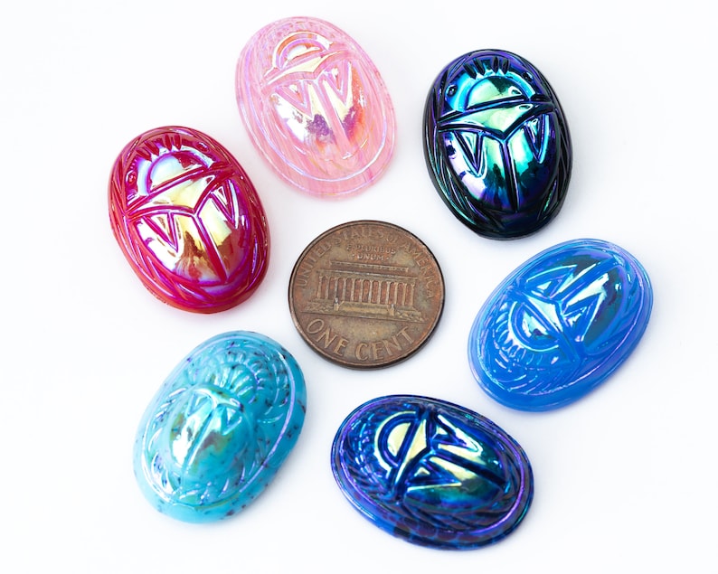 May include: Six iridescent glass scarab beetle charms in various colors, including pink, blue, green, and red. The charms are oval-shaped and feature a detailed scarab beetle design.