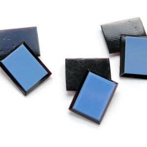 Op de afbeelding: Vijf kleine, rechthoekige, zwarte glazen tegels met een blauw reflecterend oppervlak. De tegels zijn in een willekeurig patroon op een witte achtergrond gerangschikt.