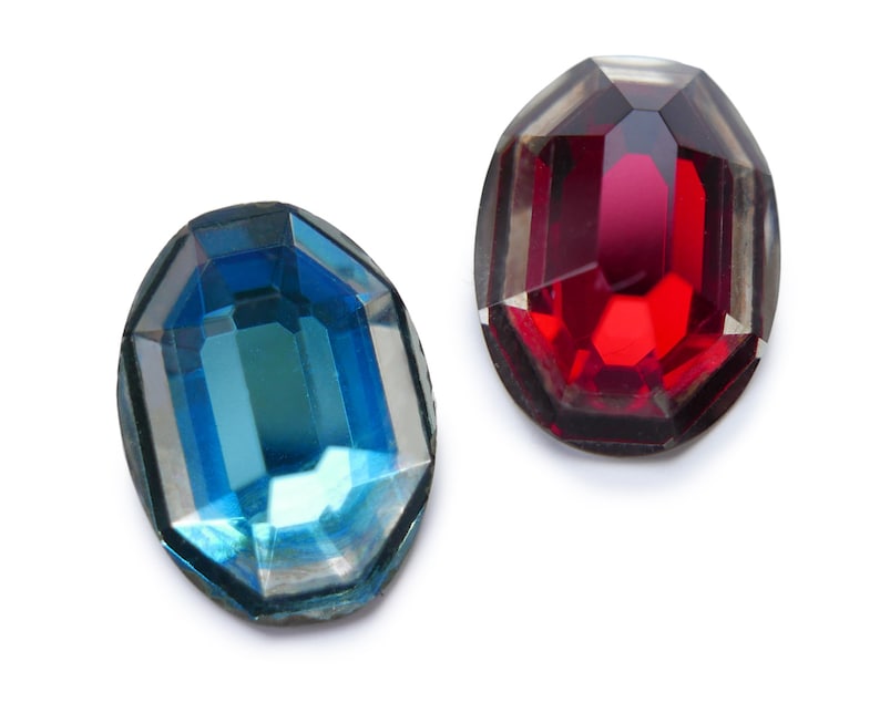 May include: Two faceted glass gems, one red and one blue, on a white background.