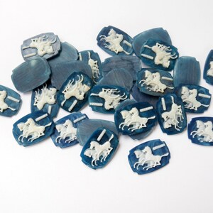 K&ouml;nnte beinhalten: Eine Sammlung von blauen und wei&szlig;en Keramikkn&ouml;pfen mit einem Design aus drei Pferden. Die Kn&ouml;pfe sind oval geformt und haben ein erhabenes Design.