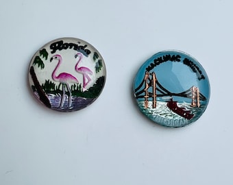 May include: Two round, vintage souvenir pins. One pin features pink flamingos and the word "Florida". The other pin depicts a bridge over water with the word "Mackinac Bridge" and "Michigan".