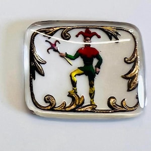 Peut inclure: Un presse-papier en verre représentant un personnage de bouffon coloré avec un chapeau rouge et des vêtements verts et jaunes. Le bouffon tient un bâton surmonté d'une fleur rouge et verte. Le presse-papier est entouré d'un cadre orné de couleur dorée.