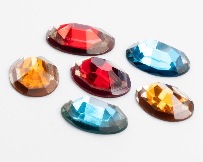 May include: Six oval-shaped rhinestones in various colors, including red, orange, and blue. The rhinestones are arranged in a semi-circle on a white background.