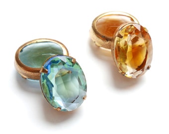Può includere: Due gemelli dorati in stile vintage. Uno presenta una grande gemma ovale, sfaccettata, blu-verde. L'altro gemello ha una gemma giallo dorato. I gemelli sono su sfondo bianco.