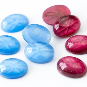 Puede incluir: Una colección de ocho piedras preciosas cabujón de forma ovalada. Cuatro son de color azul oscuro y cuatro son de color rojo oscuro. Las piedras preciosas tienen un patrón en forma de estrella en su superficie.