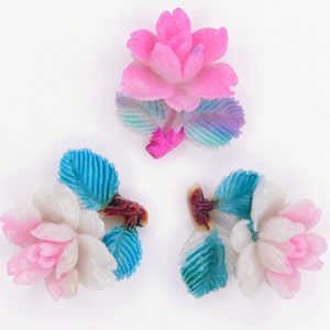 May include: Three decorative flower embellishments with pink and white petals and blue and green leaves. The flowers are made of a smooth, glossy material.