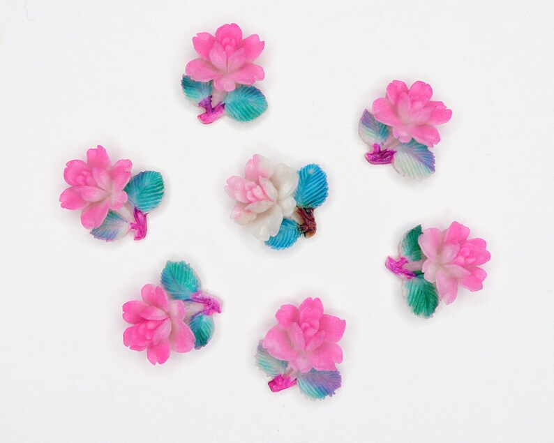 May include: Seven pink and white ceramic flower embellishments with blue and green painted leaves. The flowers have a 3D design and are perfect for adding a touch of whimsy to crafts.