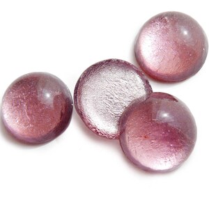 Puede incluir: Cuatro cabujones redondos de vidrio iridiscente en tonos rosa y morado. Los cabujones tienen un brillo metálico y son perfectos para la elaboración de joyas u otros proyectos decorativos.