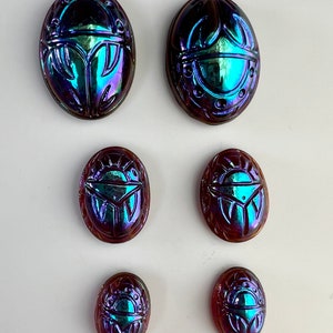 May include: Six iridescent glass scarab beetles in various sizes. The beetles are oval shaped and have a blue, green, and purple iridescent finish.