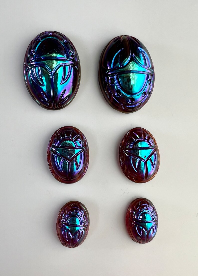 May include: Six iridescent glass scarab beetles in various sizes. The beetles are oval shaped and have a blue, green, and purple iridescent finish.