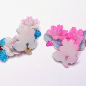 May include: Two sets of pink and white flower-shaped resin embellishments with blue and iridescent accents. The embellishments are perfect for adding a touch of whimsy to crafts and projects.