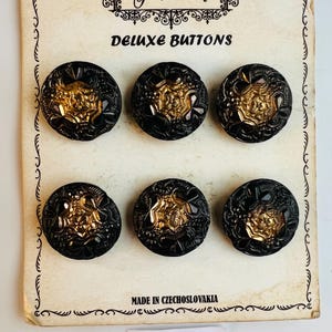 May include: A card with six black and gold buttons with a decorative design. The card reads "Fairy Queen Deluxe Buttons" and "Made in Czechoslovakia". The card also has a handwritten label that reads "MR 2".