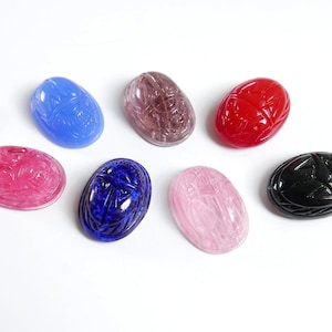 May include: Seven scarab beetle shaped cabochons in various colors, including pink, red, blue, black, and purple. The cabochons are all oval shaped and have a smooth, polished finish.