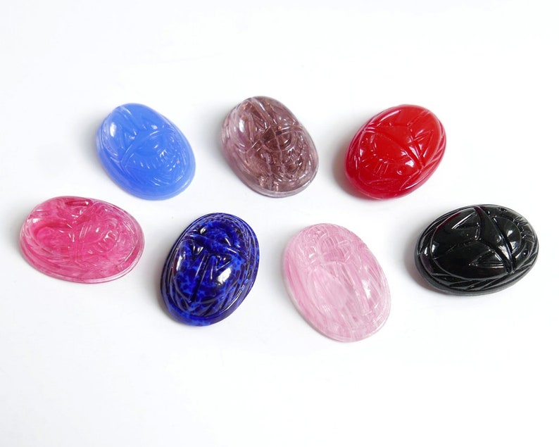 May include: Seven scarab beetle shaped cabochons in various colors, including pink, red, blue, black, and purple. The cabochons are all oval shaped and have a smooth, polished finish.