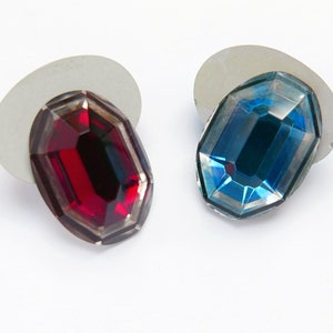 May include: Two oval-shaped glass rhinestones, one red and one blue, on white backgrounds.