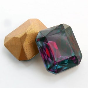 May include: Two faceted gemstones, one gold and one iridescent purple, green, and blue.