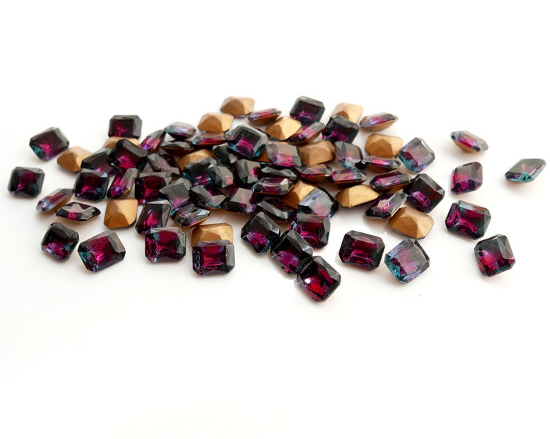 May include: A pile of dark purple and iridescent square-shaped rhinestones with gold settings.