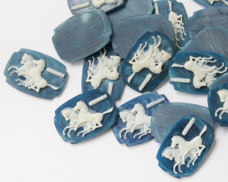 K&ouml;nnte beinhalten: Eine Sammlung von blauen und wei&szlig;en Keramikkn&ouml;pfen mit einem Design von drei galoppierenden Pferden. Die Kn&ouml;pfe sind oval geformt und haben eine glatte, gl&auml;nzende Oberfl&auml;che.
