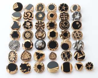 May include: A collection of 40 black and gold buttons with various designs. The buttons are round and have a shiny finish.