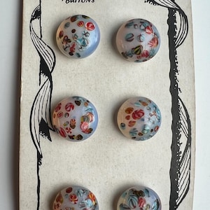 May include: Six vintage Donna Buttons on a card. The buttons are round, with a light blue base and colourful floral patterns in red, pink, and green. The card has a decorative black border and the text "Donna / Buttons".