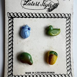 Könnte beinhalten: Vintage Karte mit vier dekorativen Knöpfen. Die Knöpfe sind geformt wie eine blaue Maus, eine grüne Ente, eine grüne Mango und eine gelbe Ananas. Die Karte trägt den Text "Latest Style" und "Made in Czechoslovakia".